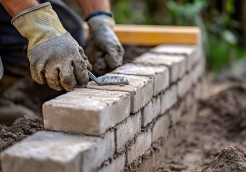 Mason laying bricks for a garden wall in a residential backyard. Featuring bricklaying technique